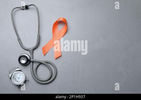 Orange ribbon, stethoscope and alarm clock on light grey table, flat lay with space for text. Multiple sclerosis awareness Stock Photo