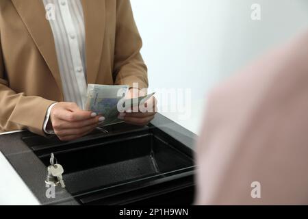 Cashier with money at currency department window in bank, closeup Stock Photo