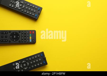 Remote controls on yellow background, flat lay. Space for text Stock Photo