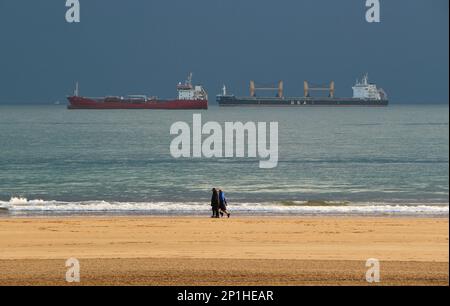 People walking on the beach with anchored ships waiting to enter the port of Santander Cantabria Spain on a winter morning Stock Photo