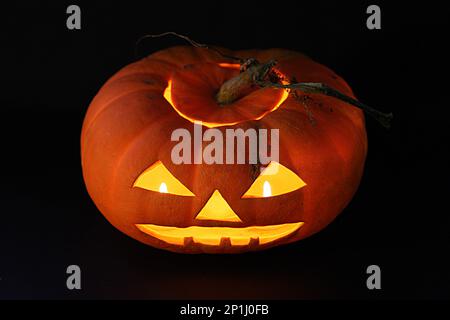 Close-up on a Jack O' Lantern lit in the dark and reflecting on a black surface in front of it. Stock Photo