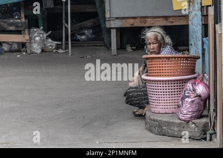 SAMUT PRAKAN, THAILAND, FEB 17 2023,  An old woman sits on the street next to a empty baskets Stock Photo