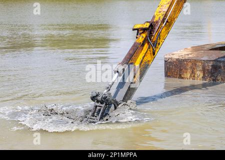 The arm of the floating dredger is dredging the bottom of the pond Stock Photo