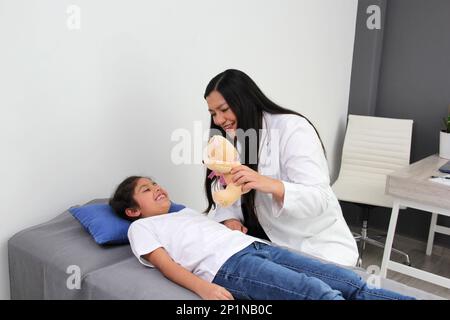 Latino pediatrician doctor checks her girl patient with autism spectrum disorder ASD, she communicates through his teddy bear that she carries as an a Stock Photo