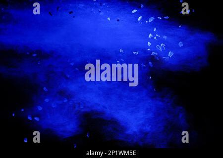 Split debris of stone exploding with blue  powder against black background. Stock Photo
