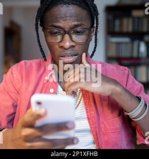 Sociable engrossed African American man holding mobile phone chatting with girlfriend via SMS Stock Photo
