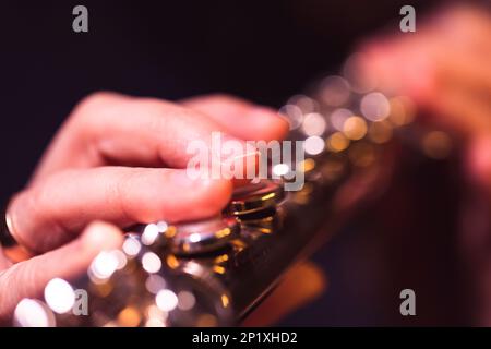 A close up portrait of fingers pressing down on the metal valves of a silver flute by a flutist playing the notes of a beautiful musical master piece. Stock Photo