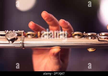 A portrait of the fingers of a hand of a flutist musician releasing the pressed valves of a metal silver flute to play a note of a musical piece durin Stock Photo
