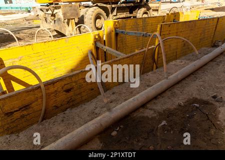 Excavator filling deep excavation supported by trench box with pipe bedding pea gravel during installation of drainage pipe. Reconstruction of technic Stock Photo