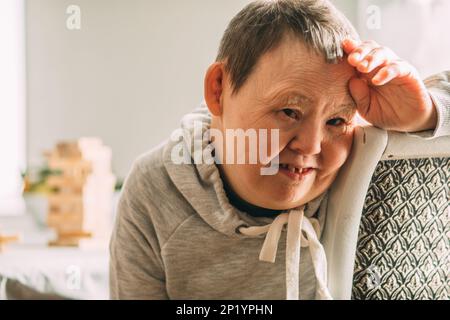 Portrait of an elderly smiling woman with Down syndrome in a sunny room Stock Photo