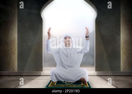 Muslim man sitting while raised hands and praying in the mosque Stock Photo