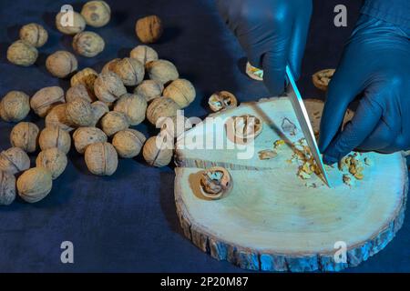 Chef in gloves chops walnuts with a knife on a wooden board. Stock Photo