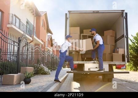 Workers unloading boxes from van outdoors. Moving service Stock Photo