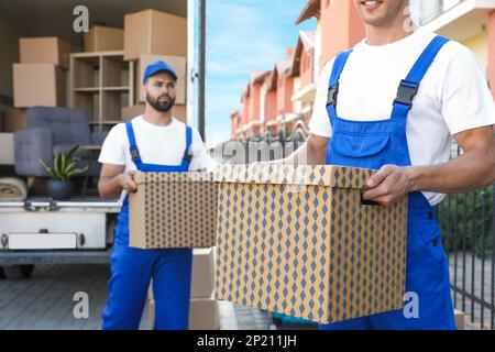 Workers unloading boxes from van outdoors. Moving service Stock Photo