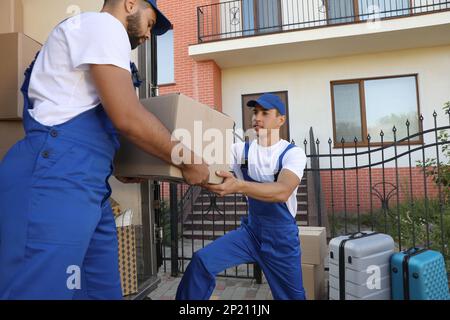 Moving service workers unloading boxes near house Stock Photo