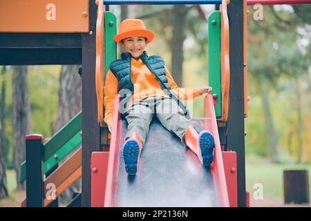Happy little boy slides down the slide at the children's playground. Stock Photo