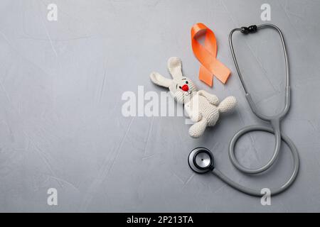 Orange ribbon, toy bunny and stethoscope on light grey table, flat lay with space for text. Multiple sclerosis awareness Stock Photo