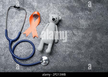 Orange ribbon, toy bear and stethoscope on grey table, flat lay with space for text. Multiple sclerosis awareness Stock Photo