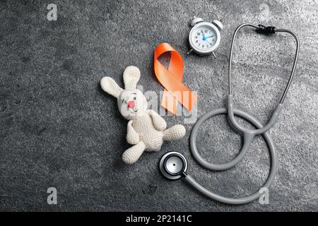 Orange ribbon, toy bunny, stethoscope and alarm clock on grey table, flat lay with space for text. Multiple sclerosis awareness Stock Photo