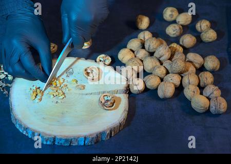Chef in gloves chops walnuts with a knife on a wooden board. Stock Photo