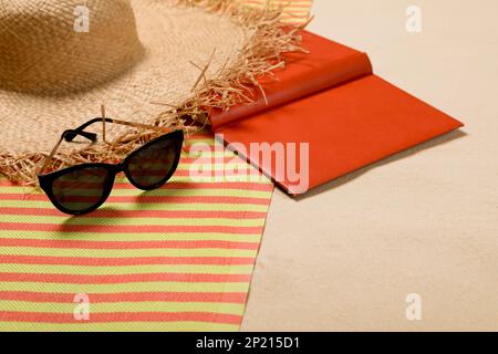 Striped beach towel, hat, book and sunglasses on sand, closeup Stock Photo