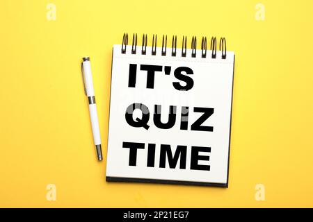 Phrase It's quiz time written in notebook and pen on yellow background, flat lay Stock Photo