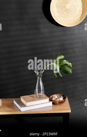 monstera leaf in vase, books and shells on bench Stock Photo
