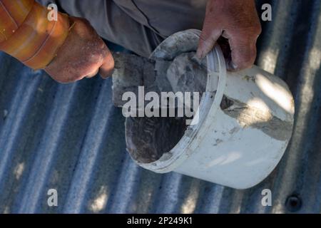 A man is sitting on the roof and filling the bucket with cement mortar. selective focus Stock Photo