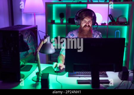 Young redhead man streamer playing video game using computer at gaming room Stock Photo