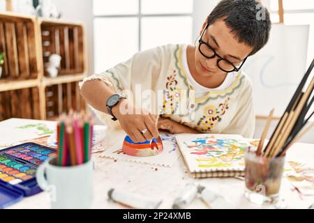 Young hispanic woman painting clay ceramic at art studio Stock Photo