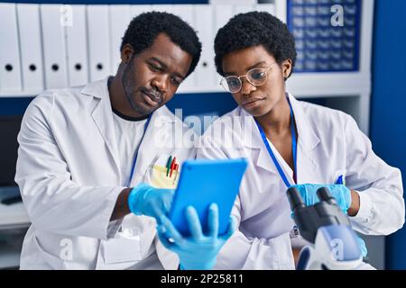 African american man and woman scientists using touchpad working at laboratory Stock Photo