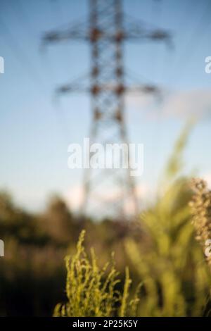 Electricity tower in the field on a sunny day out of focus. Blurred power line silhouette. Colorful landscape - blue sky and green grass defocused Stock Photo