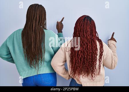 Two african woman standing over blue background posing backwards pointing ahead with finger hand Stock Photo