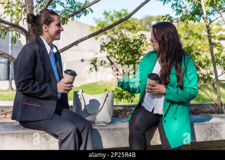 Female co-workers talking while relaxing outdoors during a coffee break. Stock Photo