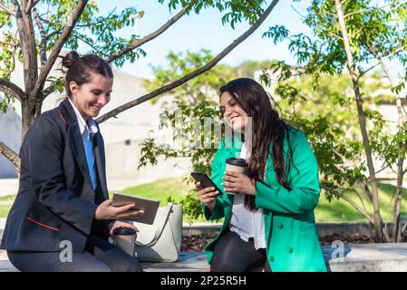 Co-workers using mobile phone and digital tablet while having a coffee break outdoors. Stock Photo