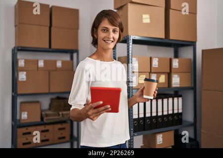 Young beautiful hispanic woman ecommerce business worker using touchpad drinking coffee at office Stock Photo