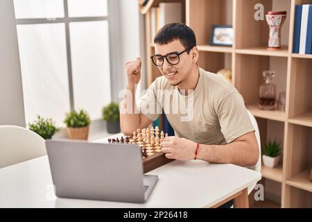 Young arab man playing chess online pointing thumb up to the side smiling happy with open mouth Stock Photo