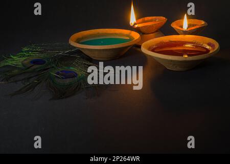 happy holi celebration with colors, clay lamp and peacock feather symbolizing hindu god krishna. Holi or dol yatra is widely celebrated across india a Stock Photo