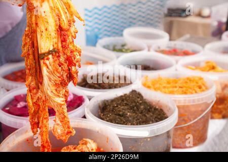 Hand holding traditional Korean dish kimchi made of napa cabbage leaves. Different pickled salads at food market stall Stock Photo