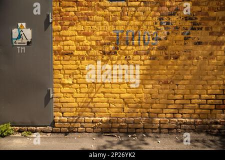 Vibrant yellow brick wall background with a door and a high voltage danger sign. Dirty grunge industrial backdrop with signs, letters and numbers Stock Photo