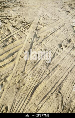 Many tire tracks and footprints in different directions on the beach sand. Tyre traces texture background Stock Photo