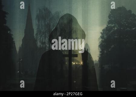 A spooky double of exposure of a mysterious silhouette of a hooded figure. With a scary graveyard and church in the background. On an eerie foggy wint Stock Photo