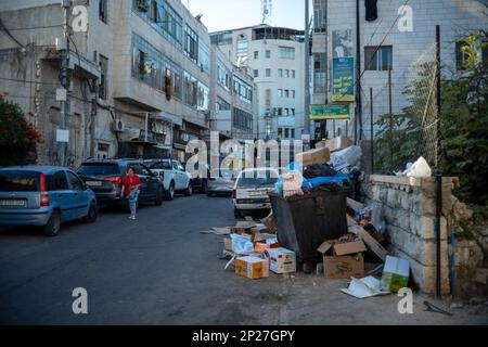 Ramallah, Ramallah and al-Bireh Governorate, Palestine, 8 July 2022: Thrash Can and Garbage by a Street of the Old Town with Buildings and Cars Parked Stock Photo