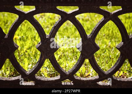 Old black cast fence on a green lawn background. Antique wrought iron fence with ornamental pattern of circles Stock Photo