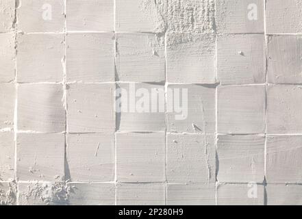 Square tiles ceramic painted white rough textured wall pattern in a sunlight background Stock Photo