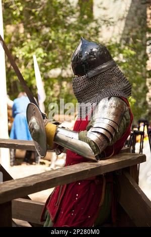 Middle ages period costume at knight tournament. Medieval historical reenactment - a man wearing metal helmet and armor suit, holding a sword Stock Photo
