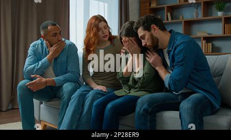 Multiracial 30s diverse people sit indoors sad crying woman sharing life problem grief. Caring friends women men consoling hugging provide Stock Photo