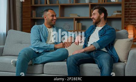 Two diverse 30s men businessmen talking at home on sofa multiracial friends companions african american caucasian ethnicity fellows brothers Stock Photo