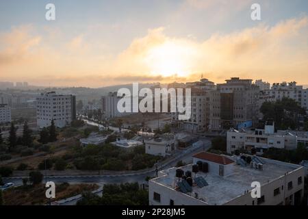 Ramallah Cityscape at Dawn Facing the Sunset, with its High White Classical Buildings and Trees Against Orange Sky Stock Photo