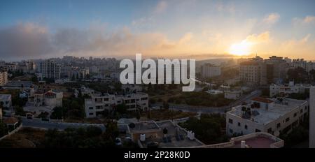 Ramallah Cityscape Panorama at Dawn with Sunset, High Buildings, and Trees Facing the Sun Stock Photo